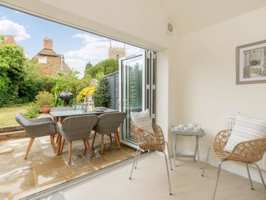 A dining area with wicker chairs and a table set inside opening to an outdoor patio with a dining table and barbecue at Holly Cottage Middle Tysoe