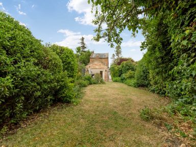 A garden with grass lawn and trees surrounding a brick house at Holly Cottage Middle Tysoe in Tysoe
