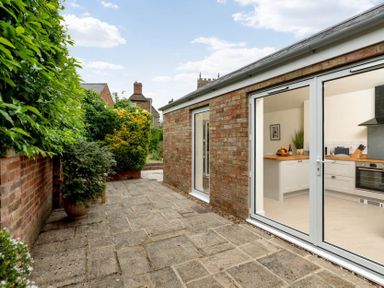 A stone patio with potted plants next to a brick building with glass doors showing a kitchen at Holly Cottage Middle Tysoe in Tysoe