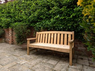 A wooden bench on a paved patio next to a brick wall with green bushes at Holly Cottage Middle Tysoe in Tysoe