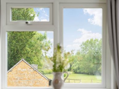 A window with a view of trees a field and a stone building with flowers in a vase in the foreground at Holly Cottage Middle Tysoe Tysoe