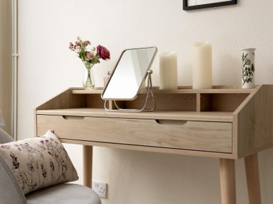 A wooden desk with a mirror, candles, and a vase with flowers beside a chair with a patterned cushion at Holly Cottage Middle Tysoe in Tysoe