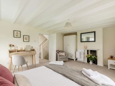 A bedroom with a bed towels a desk and chair a wardrobe an armchair and a fireplace at Holly Cottage Middle Tysoe in Tysoe