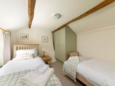 A bedroom with two single beds a wooden side table and a built-in wardrobe at Holly Cottage Middle Tysoe in Tysoe