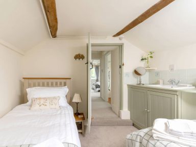 A bedroom with a single bed a bedside table with a lamp a door leading to a hallway and a cabinet with a sink at Holly Cottage Middle Tysoe in Tysoe