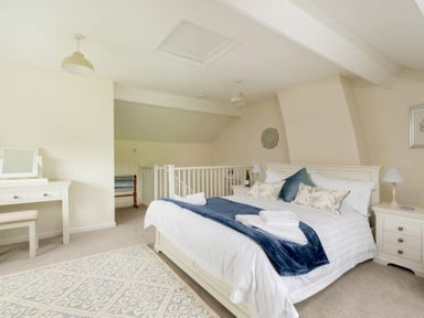 A bedroom with a double bed a blue throw and pillows bedside tables and a dressing table at Holly Cottage Middle Tysoe in Tysoe