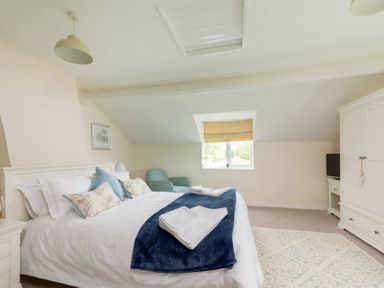 A bedroom with a bed with pillows and folded towels a chair a window a wardrobe and a television at Holly Cottage Middle Tysoe in Tysoe