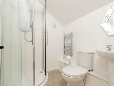 A bathroom with a curved glass shower, a toilet, a small sink, and a wall-mounted towel radiator at Holly Cottage Middle Tysoe in Tysoe