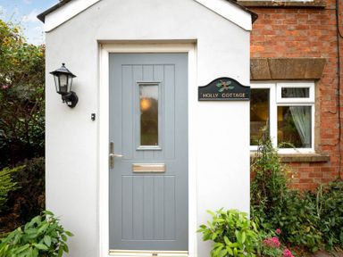 A blue front door with a small window and letterbox on a white exterior wall next to a window and garden at Holly Cottage Middle Tysoe