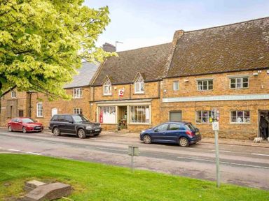 A street with parked cars and old stone buildings with a green tree in the foreground at Holly Cottage Middle Tysoe in Tysoe