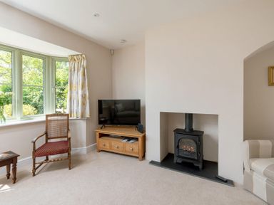 A living room with a wood burning stove television chair and window with curtains at Mount View in Childswickham