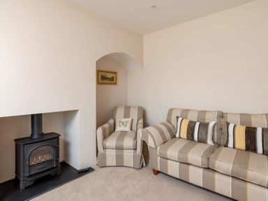 A living room with a striped armchair and sofa next to a black wood stove at Mount View in Childswickham