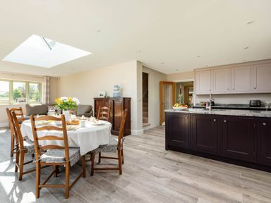 An open kitchen and dining area with a round table set for breakfast and wooden chairs in Mount View in Childswickham