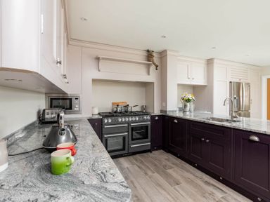A kitchen with marble countertops dark lower cabinets beige upper cabinets stove and refrigerator at Mount View in Childswickham