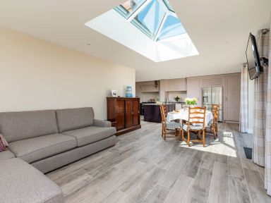 A living room with a sofa a wooden cabinet and a dining table with chairs under a skylight at Mount View in Childswickham