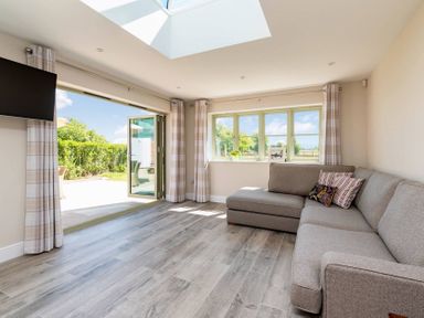 A living room with a gray sectional sofa and large windows overlooking a garden at Mount View in Childswickham
