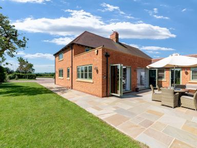 A brick house with several windows and a patio with outdoor furniture and an umbrella surrounded by a lawn at Mount View in Childswickham