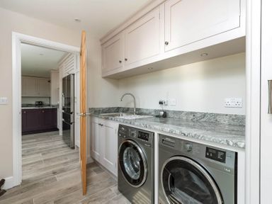 A laundry room with a washing machine and dryer under a countertop and cabinets above at Mount View in Childswickham