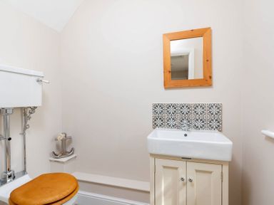 A bathroom with a toilet wooden seat a white sink under a wooden framed mirror and patterned tiles at Mount View in Childswickham