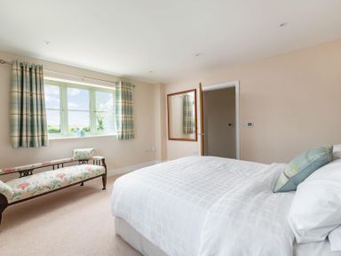 A bedroom with a bed, patterned bench, window with curtains and a wall mirror at Mount View in Childswickham
