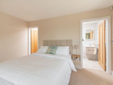 A bedroom with a double bed a bedside table with a lamp and an en suite bathroom at Mount View in Childswickham