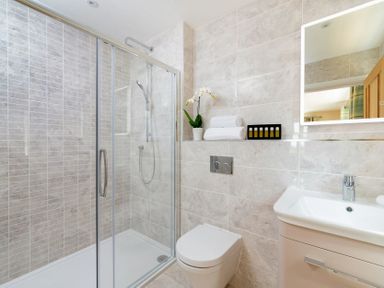 A bathroom with a glass enclosed shower a wall mounted toilet a sink with faucet a mirror and towels on a shelf at Mount View in Childswickham
