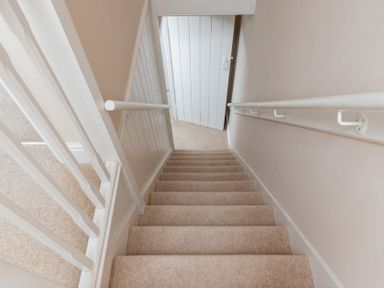 A carpeted staircase with white banisters and handrails leading down to a white door at Mount View in Childswickham
