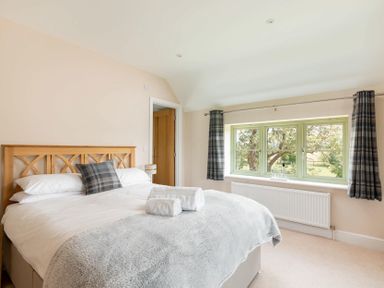 A bedroom with a wooden headboard bed with white bedding and gray throws near a window with plaid curtains at Mount View in Childswickham