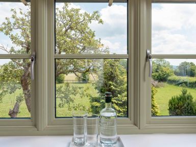 A window looking out to trees and grass with a tray holding a bottle and two glasses of water at Mount View in Childswickham