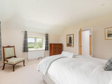 A bedroom with a bed a wooden chair a chest of drawers a window with curtains and a mirror on the wall at Mount View in Childswickham