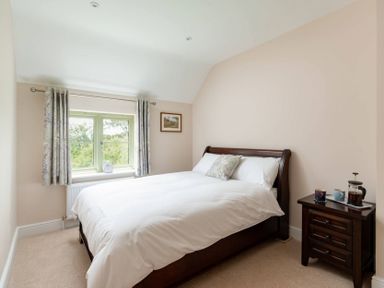 A bedroom with a double bed white bedding a window with curtains and a wooden nightstand at Mount View in Childswickham