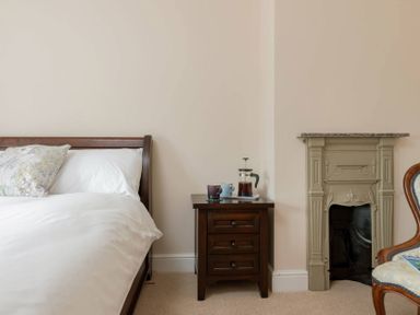 A bed with white bedding next to a wooden nightstand with a coffee press and cups by a decorative fireplace at Mount View in Childswickham