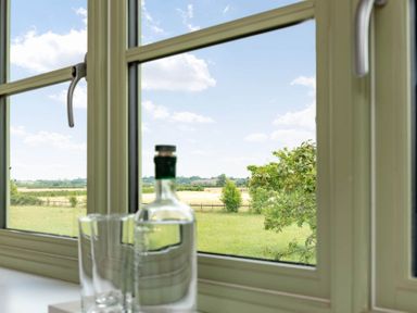 A window overlooking a grassy field and trees with a bottle and two glasses on the windowsill at Mount View Childswickham