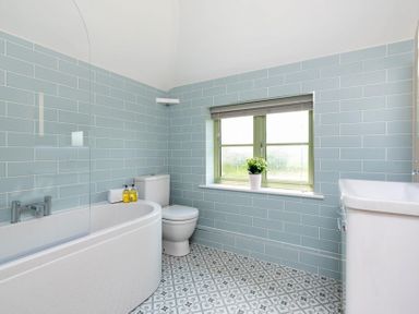 A bathroom with a bathtub toilet and sink with blue tiled walls and patterned floor at Mount View in Childswickham