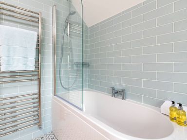 A bathroom with a bathtub shower combination with glass screen towel rack and soap dispensers at Mount View in Childswickham