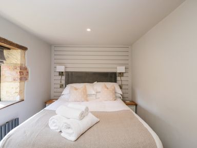 A bedroom with a double bed with pillows and rolled towels on the bed at Millbank Cottage in Mickleton