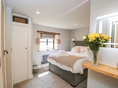 A bedroom with a bed towels on bed window with blind flowers on wooden shelf at Millbank Cottage in Mickleton