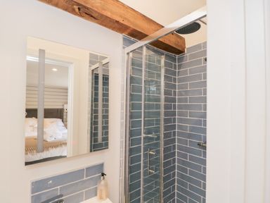 A bathroom with a glass shower enclosure and blue tiled walls showing a reflection of a bedroom at Millbank Cottage in Mickleton