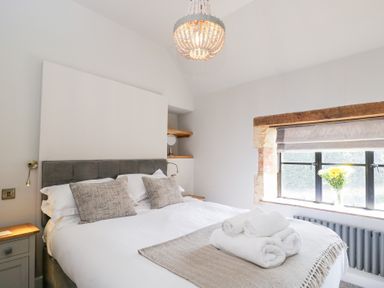 A bedroom with a double bed towels on bed and a window with flowers at Millbank Cottage in Mickleton