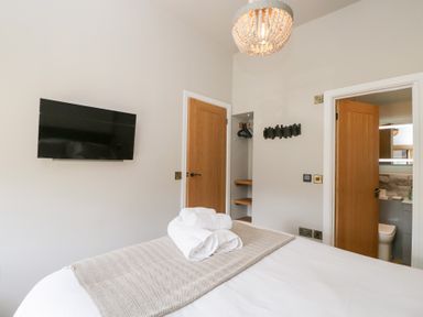 A bedroom with a bed with towels on it a wall-mounted television wooden doors and an open door to a bathroom at Millbank Cottage in Mickleton