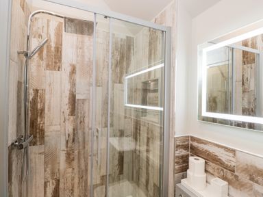 A bathroom with a glass shower enclosure and a wooden tiled wall at Millbank Cottage in Mickleton