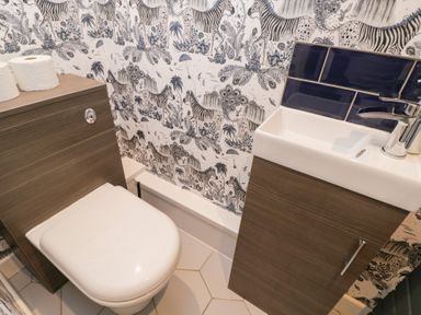 A bathroom with a toilet and a small sink with cabinets and animal patterned wallpaper at Millbank Cottage in Mickleton