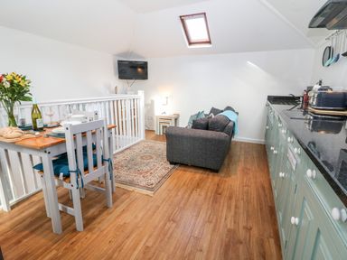 An open plan kitchen and living area with a dining table set for two a sofa and a wall mounted television at The Bath House in Blockley