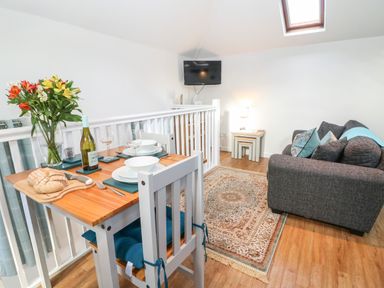 A dining table set with plates glasses bread and wine next to a gray sofa with cushions and a rug in a living area at The Bath House in Blockley