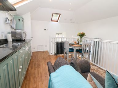 A kitchen with mint green cabinets a wooden floor and a dining table with chairs and flowers at The Bath House in Blockley