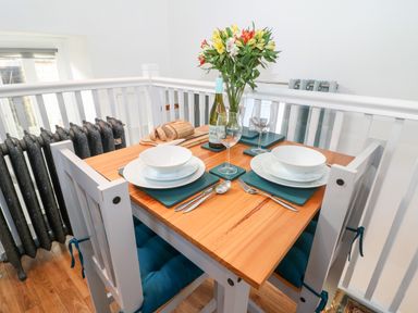 A dining table set with plates bowls cutlery wine glasses a bottle of wine and a vase of flowers at The Bath House in Blockley