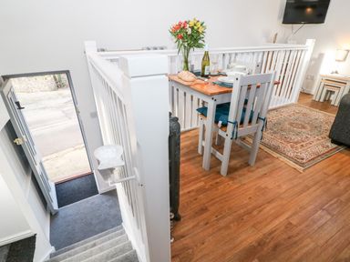 A dining table with chairs and plates beside a staircase with an open door at The Bath House in Blockley