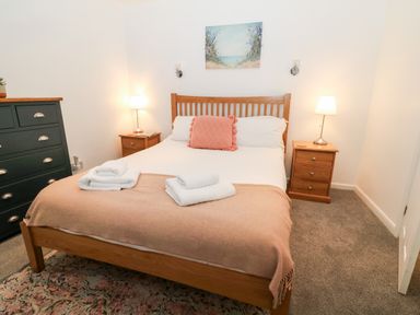 A bedroom with a wooden double bed two bedside tables with lamps a green chest of drawers and a rug at The Bath House in Blockley