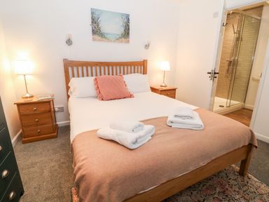 A bedroom with a wooden bed a pink cushion bedside tables with lamps and an en suite bathroom at The Bath House in Blockley
