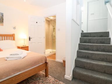 A bedroom with a wooden bed and bedside table next to a bathroom door and carpeted stairs at The Bath House in Blockley